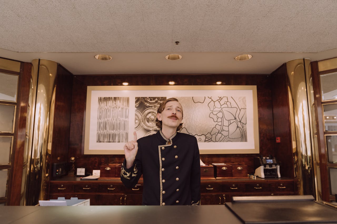 A luxury hotel receptionist in uniform stands behind the opulent front desk, ready to assist guests.